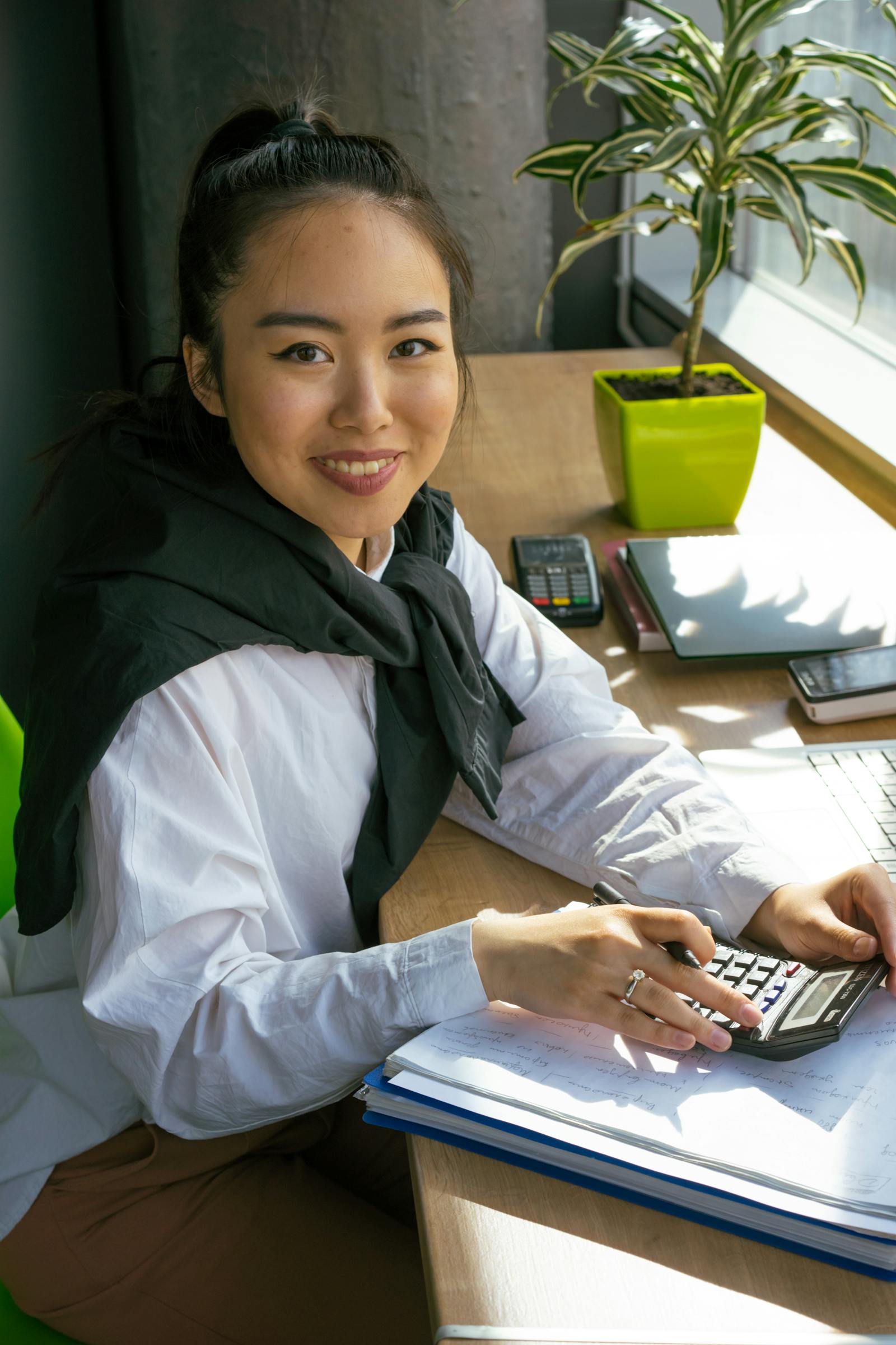Asian SME owner running AutoCount Accounting 2.0 with calculator and laptop on desk